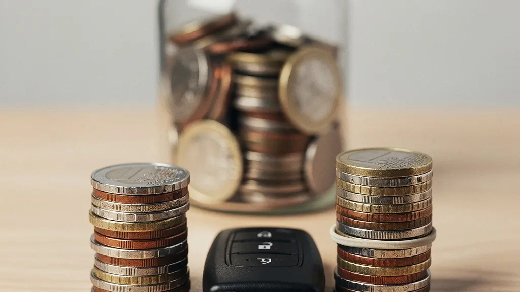 Deux piles de pieces en euros et une cle de voiture sur une table, avec un bocal d epargne en arriere-plan flou, symbolisant l arbitrage entre prime et franchise.